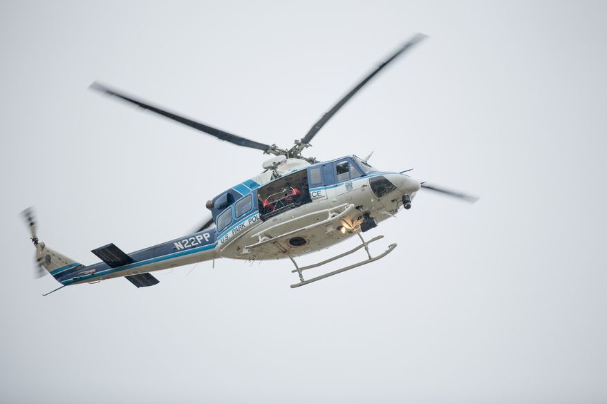 ** FILE ** A rifleman sits inside a helicopter circling above the Washington Navy Yard as police search for shooters on Monday, Sept. 16, 2013. (Andrew S. Geraci/The Washington Times)