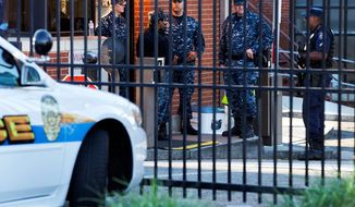 An officer who said he was with the Department of Defense (right) and Navy personnel stand guard inside the gate of the closed Washington Navy Yard on Tuesday. (ASSOCIATED PRESS)