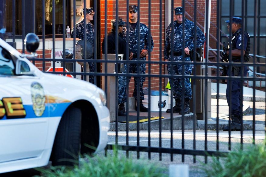 An officer who said he was with the Department of Defense (right) and Navy personnel stand guard inside the gate of the closed Washington Navy Yard on Tuesday. (ASSOCIATED PRESS)