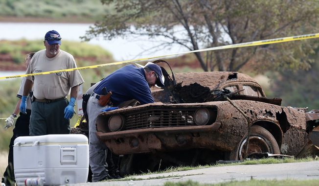 Law enforcement officials from multiple agencies examine the two cars pulled from Foss Lake, in Foss, Okla., Wednesday, Sept. 18, 2013. The Oklahoma State Medical Examiner’s Office says authorities have recovered skeletal remains of multiple bodies in the Oklahoma lake where the cars were recovered. (AP Photo/Sue Ogrocki)