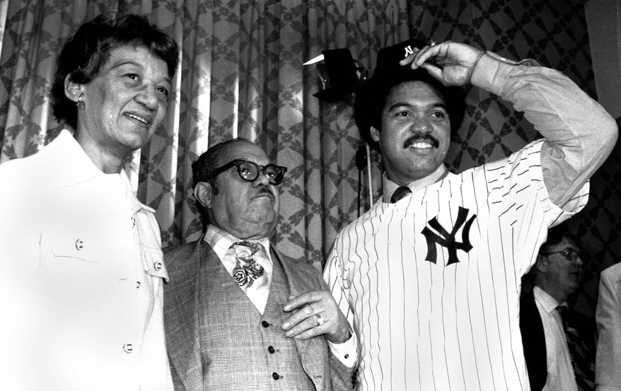 Mr. and Mrs. Martinez Jackson, left, look on as their son Reggie models his New York Yankee uniform for the press on Nov. 29, 1976 after the announcement that he signed a $3 million, five year contract with the Yanks. (AP Photo)
