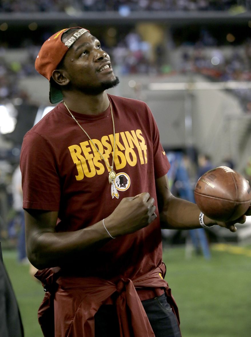 Oklahoma City Thunder's Kevin Durant stands on the sideline peering up at the large video screen playing with a football as the Redskins and Dallas Cowboys warm up before an NFL football game, Sunday, Oct. 13, 2013, in Arlington, Texas. (AP Photo/Tim Sharp)
