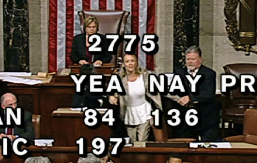 In this image from House Television, with partial voting totals on the screen, a woman, at the rostrum just below the House presiding officer, seen between the "yea" and "nay" wording, is removed from the House chamber after she began shouting during the vote for the bill to end the partial 16-day government shutdown and to fund the government. The woman was described by lawmakers and aides as a long-time House stenographer. (AP Photo/House TV)