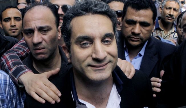 FILE - In this Sunday, March 31, 2013 file photo, a bodyguard secures popular Egyptian television satirist Bassem Youssef, who has come to be known as Egypt&#x27;s Jon Stewart, as he enters Egypt&#x27;s state prosecutors office to face accusations of insulting Islam and the country&#x27;s Islamist leader in Cairo, Egypt. After more than four months away, the man known as &amp;#8220;Egypt&amp;#8217;s Jon Stewart&amp;#8221; returns the airwaves Friday in a country radically different from the one he previously mocked. Satirist Bassem Youssef&amp;#8217;s weekly &amp;#8220;El-Bernameg,&amp;#8221; or &amp;#8220;The Program&amp;#8221; in Arabic, mocked the country&amp;#8217;s first elected Islamist president and his supporters for mixing religion and politics, took them to task for failing to be inclusive or deliver on people&amp;#8217;s demands for change_ to the extent that some said he was one of the main reasons people turned against Mohammed Morsi. (AP Photo/Amr Nabil, File)