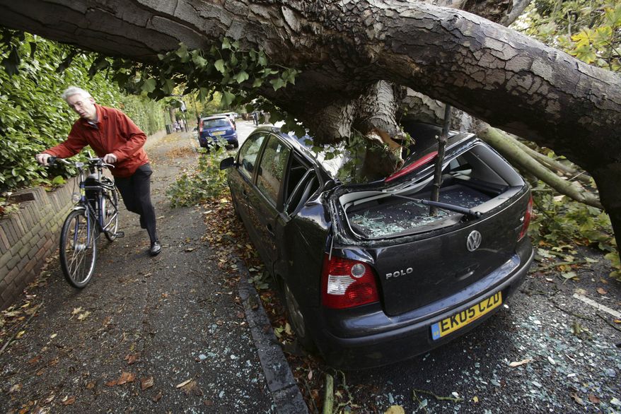 A car is crushed under a fallen tree as a man pushes a bicycle nearby following a storm, in Hornsey, north London, Monday, Oct. 28, 2013. A major storm with hurricane-force winds is lashing southern Britain, causing flooding and travel delays including the cancellation of roughly 130 flights at London's Heathrow Airport. (AP Photo/PA, Yui Mok)