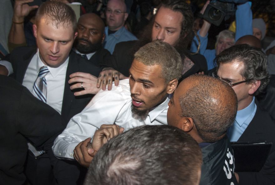 Singer Chris Brown is surrounded by bodyguards as he departs the H. Carl Moultriel courthouse Monday, Oct. 28, 2013, in Washington. A charge against the Grammy Award-winning R&B singer has been reduced to a misdemeanor and he was ordered released after his arrest Sunday following an altercation outside a Washington hotel. (AP Photo/Cliff Owen)