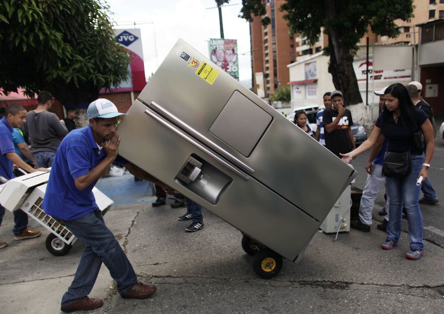 A man transports a recently purchased refrigerator on a dolly, outside an appliance store in Caracas, Venezuela, Monday, Nov. 11, 2013. President Nicolas Maduro seized control of a nationwide chain of appliance stores Friday seeking to battle inflation and shortages. Shoppers were still arriving Monday to join the hundreds who began amassing over the weekend after price inspectors said they found evidence of "usury" and Maduro ordered the chain Tiendas Daka "occupation." (AP Photo/Ariana Cubillos)