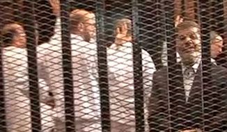 ** FILE ** Ousted President Mohammed Morsi, right, speakes from the defendant&#39;s cage as he stands with co-defendants in a makeshift courtroom during a trial hearing in Cairo, Egypt, Nov. 4, 2013. (AP Photo/Egyptian Interior Ministry, File)