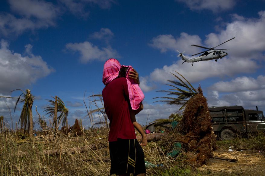 A Typhoon Haiyan survivor carries a child wrapped in a towel as he watches a helicopter landing to bring aid to the destroyed town of Guiuan, Samar Island, Philippines, Friday, Nov. 15, 2013. As an international aid effort gathered steam, resilient Filipinos in battered towns started rebuilding their lives and those of their neighbors - with or without help from their government or foreign aid groups. (AP Photo/David Guttenfelder)