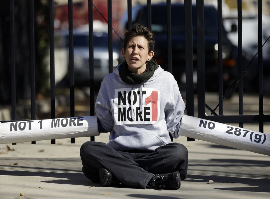 An Immigration activist, protesting deportations of people who are in the country illegally, blocks the front gate of a building that houses federal immigration authorities Tuesday, Nov. 19, 2013, in Atlanta. Eight immigration activists were taken into custody after they locked arms and some of them chained themselves to the gates outside the offices. Information on possible charges faced by the protesters wasn't immediately available. (AP Photo/John Bazemore)