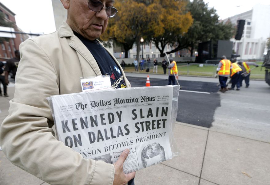 Carlos Flores holds a copy of the Dallas Morning News as work crews finish up street work on Dealey Plaza in Dallas, Thursday, Nov. 21, 2013. Loose gatherings of the curious and conspiracy-minded at Dallas’ Dealey Plaza have marked past anniversaries of the assassination of President John F. Kennedy. But for the 50th anniversary, the city of Dallas has planned a solemn ceremony Friday in the plaza he was passing through when shots rang out. There will be brief remarks by the mayor and the tolling of church bells. (AP Photo/LM Otero)