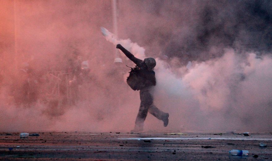 An anti-government protester throws back a tear gas canister fired by riot police in Bangkok on Sunday, Dec. 1, 2013. Police fought off mobs of rock-throwing protesters armed with petrol bombs who tried to battle their way into the government's heavily fortified headquarters as gunshots rang out in the capital and Prime Minister Yingluck Shinawatra fled a police complex during the sharpest escalation yet of the country's latest crisis. (AP Photo/Wason Wanitchakorn)