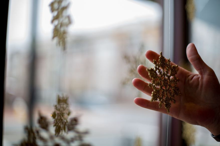 Susan Gonzalez, owner of Slaters Market, hangs gold snowflakes in her display window to signify the start of the holiday season, in Alexandria, VA., Monday, December 2, 2013. (Andrew S Geraci/The Washington Times)