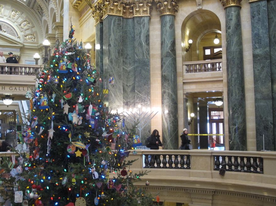 Visitors to the Wisconsin Capitol walk past a menorah and Festivus pole (right) on display in the rotunda, along with a 30-foot Christmas tree, on Thursday, Dec. 5, 2013, in Madison, Wis. The Capitol is full of displays over the holidays, including two traditional Nativity scenes and a sign calling religion nothing but a myth and superstition. (AP Photo/Scott Bauer)
