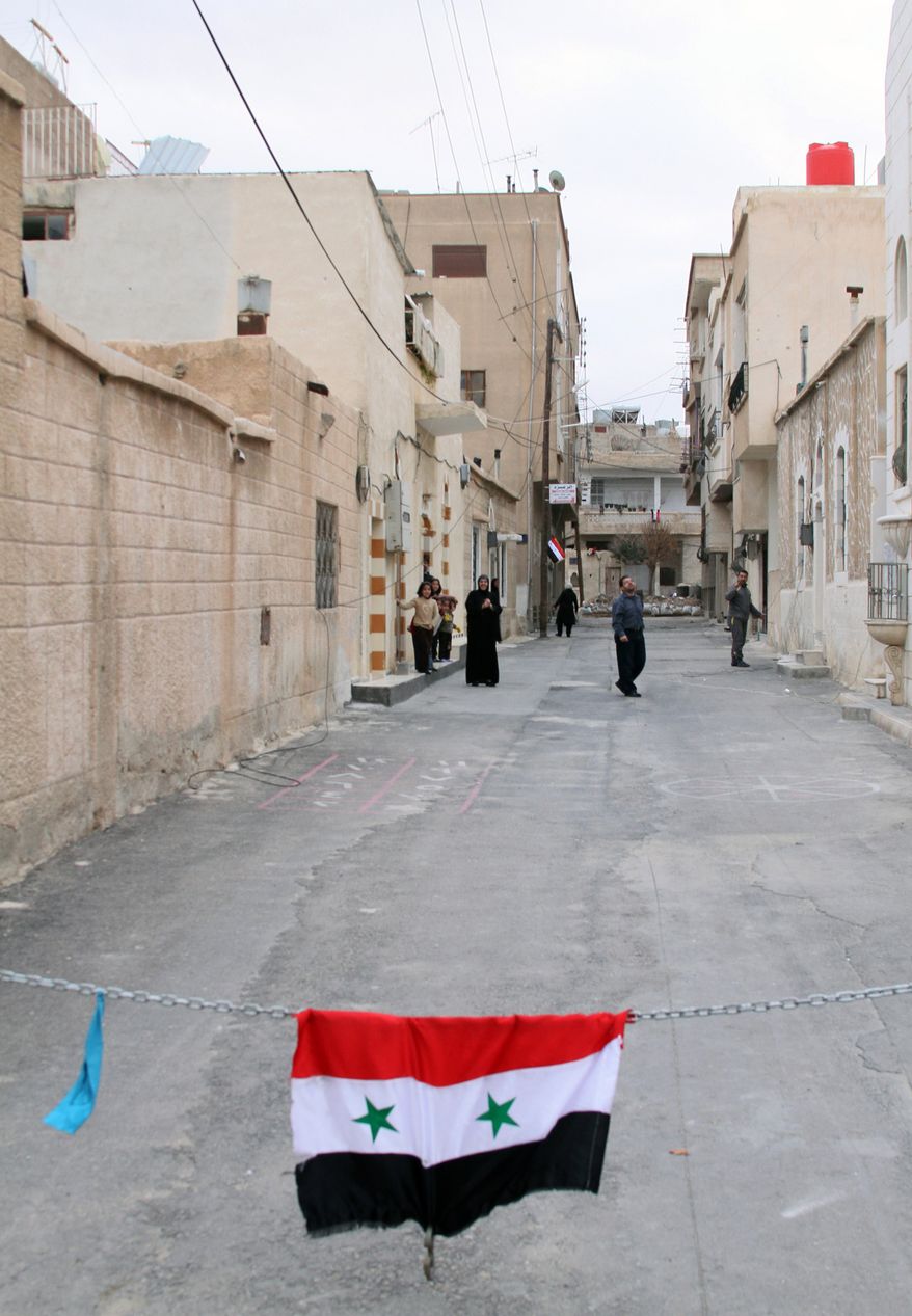 This image made on a government-organized media tour for local journalists shows a Syrian national flag hanging on a chain barrier as people return to the western town of Nabek, which Syrian troops took full control of a day earlier after taking the nearby highway that links the capital, Damascus, Syria, with the central city of Homs, Tuesday, Dec. 10, 2013. State media said that the capture of the town comes as the government forges ahead with a punishing offensive in a mountainous region near the border with Lebanon. (AP Photo)