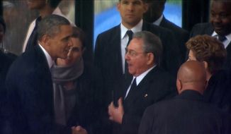 In this image from TV, U.S. President Barack Obama shakes hands with Cuban President Raul Castro at the FNB Stadium in Soweto, South Africa, in the rain for a memorial service for former South African President Nelson Mandela, Tuesday Dec. 10, 2013. (AP Photo/SABC Pool)