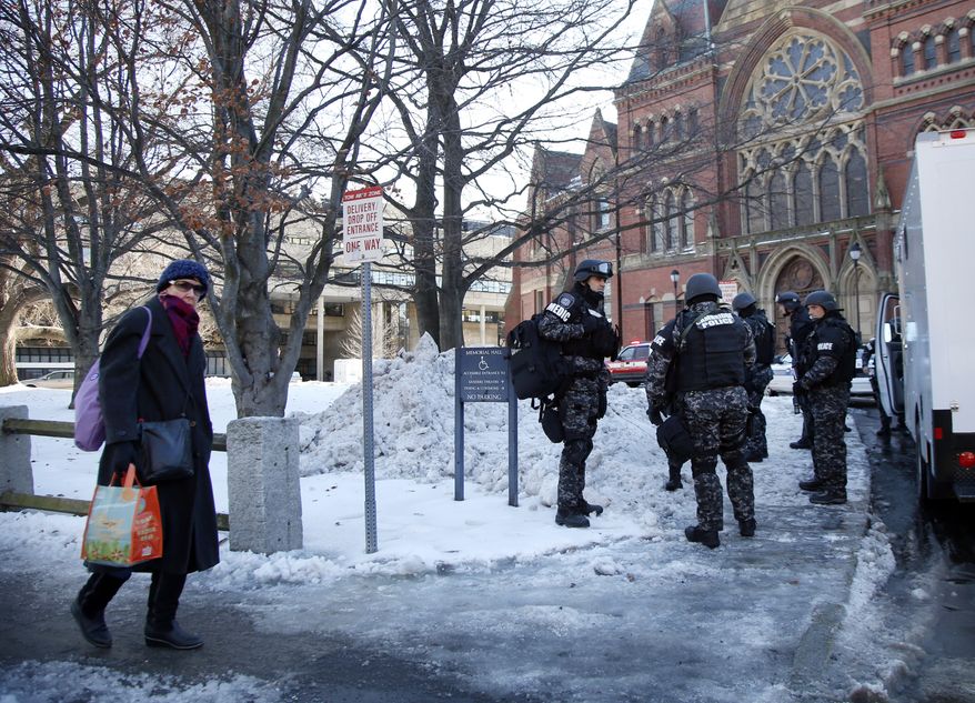 ** FILE ** A pedestrian walks by as SWAT team members assemble outside a building at Harvard University in Cambridge, Mass., Monday, Dec. 16, 2013. Four buildings on campus were evacuated after campus police received an unconfirmed report that explosives may have been placed inside, interrupting final exams. (AP Photo/Elise Amendola)