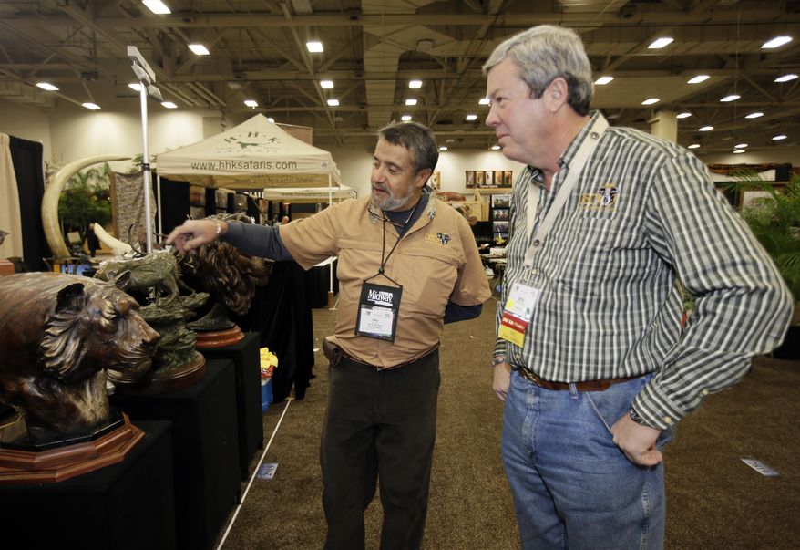 Dallas Safari Club executive director Ben Carter, right, talks with wildlife artist Raj S. Paul at his exhibit booth in the Dallas Convention Center as preparations continue for the clubs weekend show, Wednesday, Jan. 8, 2014, in Dallas. The FBI is investigating death threats made against members of the Dallas Safari Club, which intends to auction off a rare permit to hunt an endangered black rhino, an FBI spokeswoman said Wednesday. (AP Photo/Tony Gutierrez)