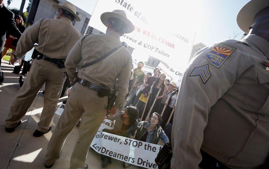 Immigration rights protesters sit in front of Department of Public Safety police officers as they block the House of Representatives entrance after Arizona Gov. Jan Brewer gives her State of the State address at the Arizona Capitol Monday, Jan. 13, 2014, in Phoenix. The Republican governor used her annual State of the State address to focus on overhauling a troubled child welfare agency, boosting the economy and changing the way schools are funded. (AP Photo/Ross D. Franklin)