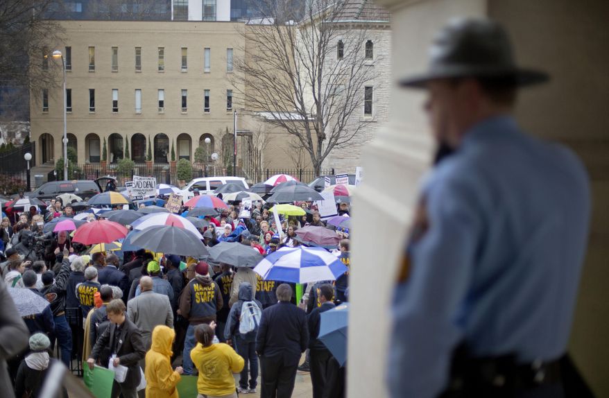 A police officer watches over a protest calling for an expansion to Medicaid outside the State Capitol on the first day of the legislative session, Monday, Jan. 13, 2014, in Atlanta. The protest marking the start of the "Moral Monday" movement in Georgia, aims to put pressure on Gov. Nathan Deal to expand Medicaid under the federal health care law. Deal has said the state can't afford the expansion. The effort includes various advocacy groups and the Georgia NAACP, and is modeled after a group in North Carolina. Demonstrators there were arrested weekly last year. (AP Photo/David Goldman)