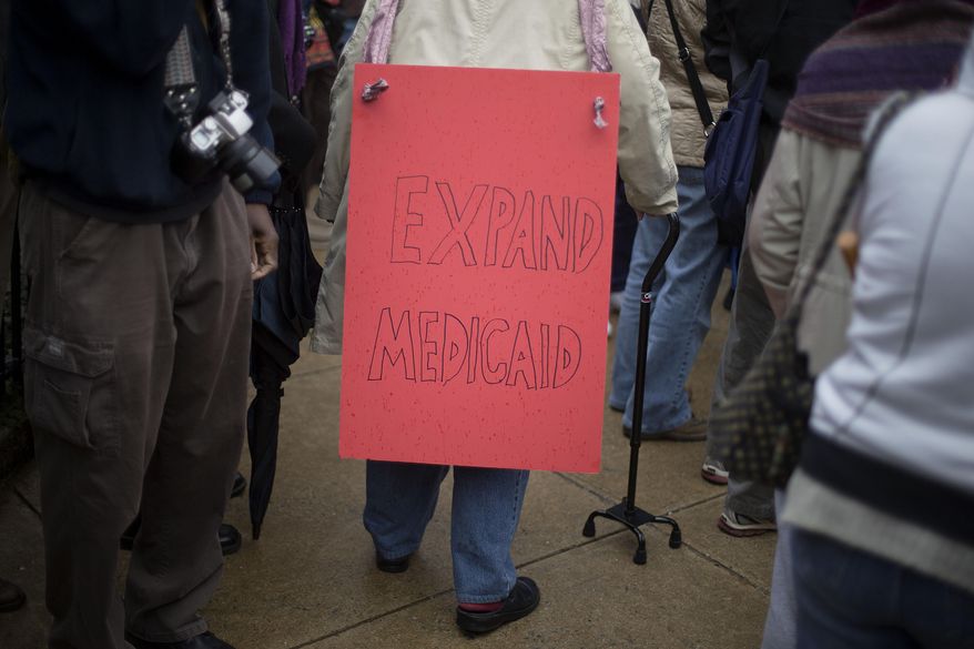 A demonstrator walks through the crowd with a sign on her back during a protest calling for an expansion to Medicaid outside the State Capitol on the first day of the legislative session, Monday, Jan. 13, 2014, in Atlanta. The protest marking the start of the "Moral Monday" movement in Georgia, aims to put pressure on Gov. Nathan Deal to expand Medicaid under the federal health care law. (AP Photo/David Goldman)