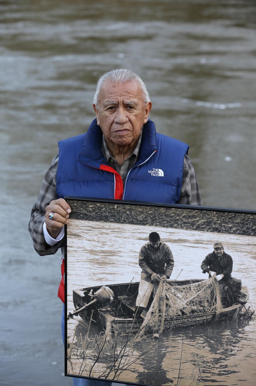 Billy Frank Jr., a Nisqually tribal elder who was arrested dozens of times while trying to assert his native fishing rights during the Fish Wars of the 1960s and '70s, poses for a photo Monday, Jan. 13, 2014, while holding a late 1960s photo of himself, left, fishing with Don McCloud, near Frank's Landing on the Nisqually River in Nisqually, Wash. Several Washington state lawmakers are pushing to give people arrested during the Fish Wars a chance to expunge their convictions from the record. (AP Photo/Ted S. Warren)