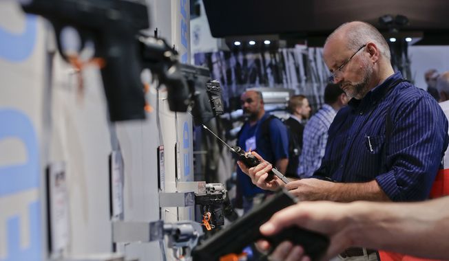 Trade show attendees examine various hand guns in the Smith &amp; Wesson display booth at the Shooting Hunting and Outdoor Tradeshow, Tuesday, Jan. 14, 2014, in Las Vegas. (AP Photo/Julie Jacobson) 
