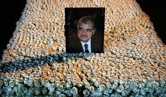 A portrait of slain Lebanese Prime Minister Rafik Hariri sits on his grave which is covered by flowers in downtown Beirut, Lebanon, Wednesday, Jan. 15, 2014. Nearly nine years after the truck bomb assassination of former Lebanese Prime Minister Rafik Hariri shook the Middle East and awakened the seeds of Sunni-Shiite hatreds, an international tribunal begins the long awaited trial of four Hezbollah suspects Thursday. The men have not been arrested, and the Hague-based court will try them in absentia in the first such trial since World War II. (AP Photo/Hussein Malla)