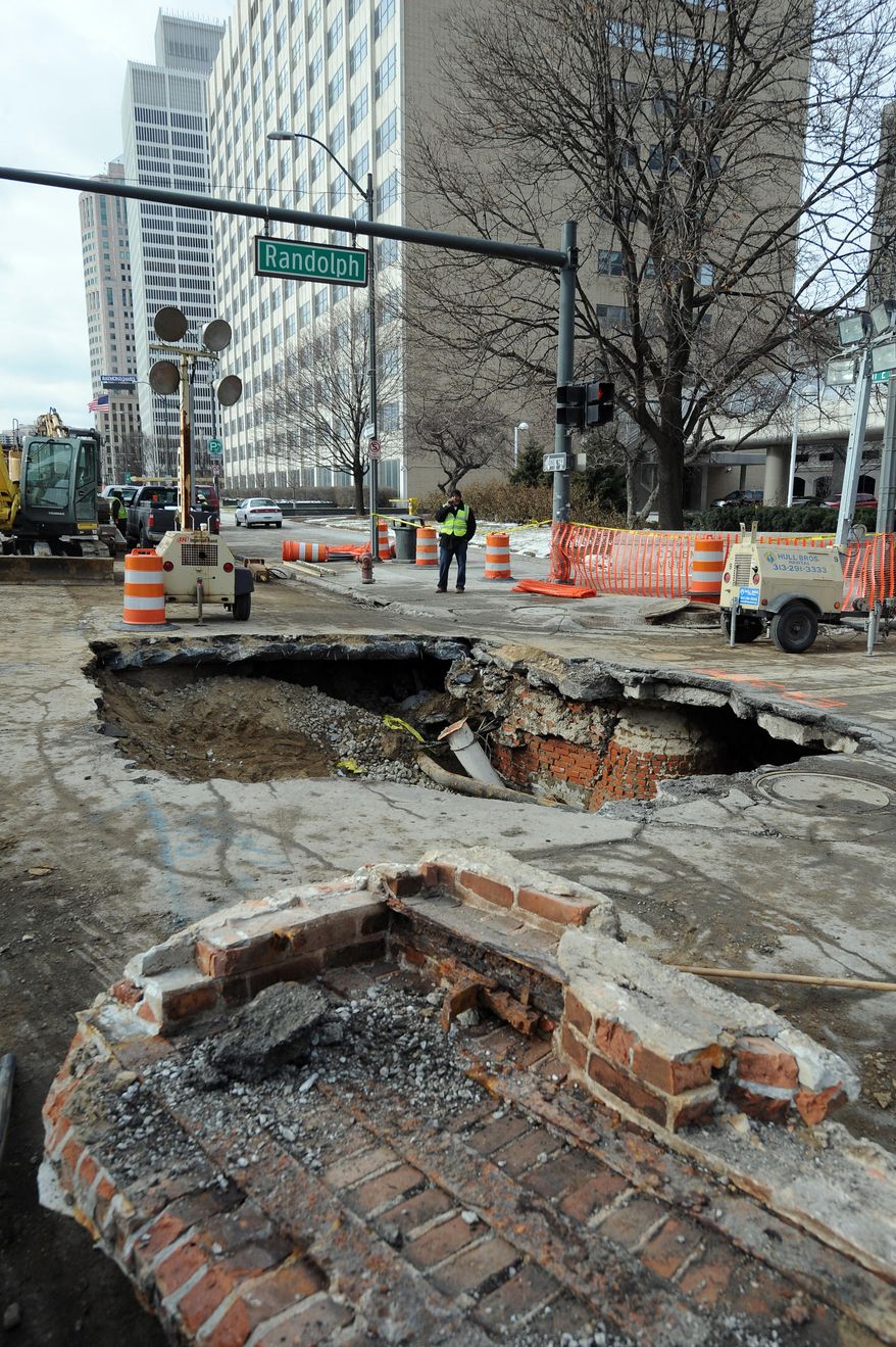 Work crews examine a 14-feet-deep sinkhole Monday, Jan. 20, 2014 that opened up in downtown Detroit over the weekend. Officials learned there was a water main break about 14 feet underground, which caused the surface to collapse, according to the Detroit News. (AP Photo/The Detroit News, Max Ortiz)