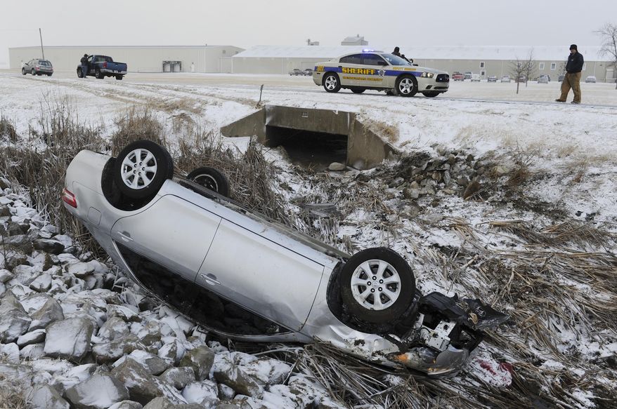 Henderson County Sheriff's deputies cover the scene after a car slid off state road 136 west and overturned into a drainage ditch, Tuesday morning, Jan. 21, 2014, in Henderson, Ky. Snow and wind brought hazardous winter conditions to a large swath of Kentucky on Tuesday, creating a slow, messy morning commute and previewing a drop in temperatures to the single digits and teens as the week wears on.(AP Photo/The Gleaner, Mike Lawrence)
