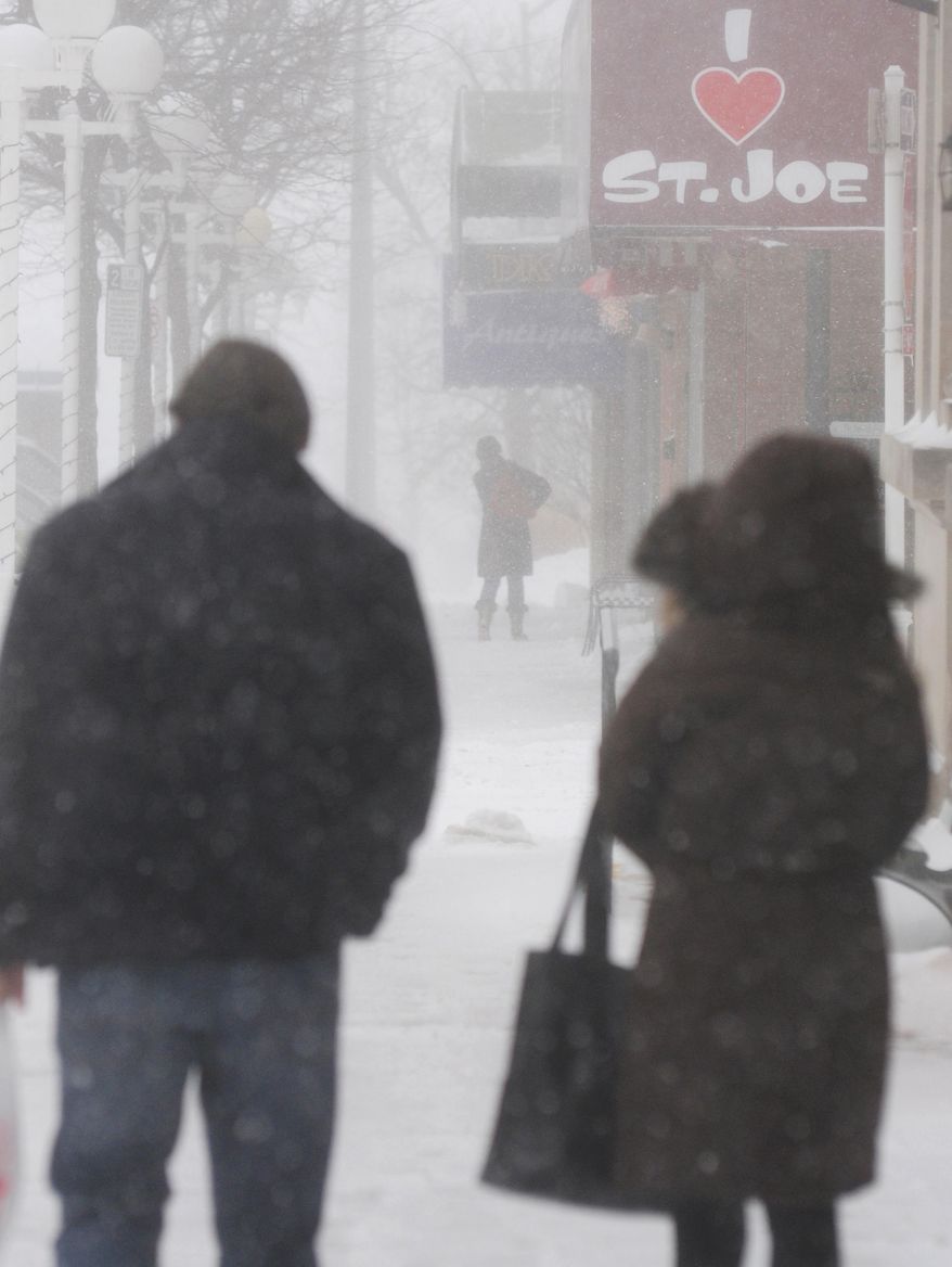 People walk through downtown St. Joesph, Mich on Saturday, Jan. 25, 2014 as snow falls. Blowing and drifting snow obscures visibility in much of the area.(AP Photo/The Herald-Palladium, Don Campbell)