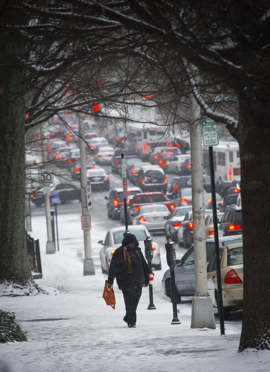 A pedestrian makes her way along a downtown sidewalk with traffic snarling behind her as people try to beat the snow accumulating on the streets Tuesday, Jan. 28, 2014, in Atlanta. Georgians stocked up on ice-melting chemicals, school systems closed, and road crews prepared to clear snow and ice from highways as a winter storm took aim. (AP Photo/John Amis)