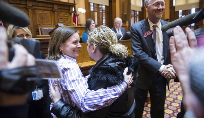 Medical marijuana advocates Shannon Cloud, left, from Smyrna, Ga., hugs Corey Lowe, as  Rep. Allen Peake, R-Macon, right, receives a congratulatory handshake after he introduced a bill to legalize medicinal marijuana after a Georgia Legislative session in the House chamber on Tuesday, Jan. 28, 2014, in Atlanta. Both Cloud and Lowe have children suffering from disease and believe marijuana can help relieve their pain. (AP Photo/John Amis)