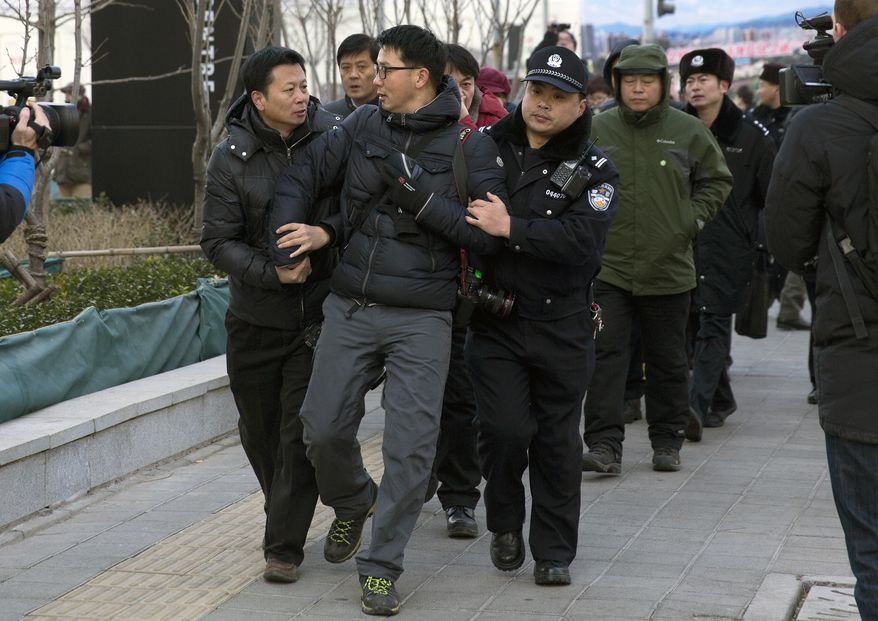 In this Sunday, Jan. 26, 2014 photo, Chinese policemen manhandle a foreign photographer, center, as he photographs Zhang Qingfang, lawyer of legal scholar and founder of the New Citizens movement Xu Zhiyong, speaking to the media near the No. 1 Intermediate People's Court, where Xu appeared for his verdict in Beijing. The government is intensifying efforts to control foreign media coverage of China, blocking websites, harassing reporters trying to cover trials of activists in Beijing and thwarting efforts by The New York Times to station new journalists on the mainland. (AP Photo/Andy Wong)