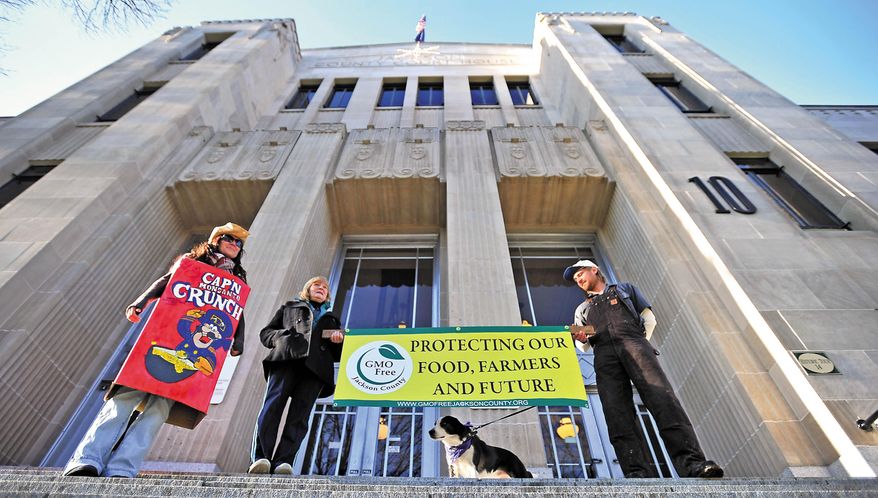 FILE - In this Jan. 2, 2013, file photo, December Tueller, left, Caroline White and Brandon Schilling, right, protest genetically modified organisms on the steps of the Jackson County Court House in Medford, Ore. Some Midwest sugar beet growers have joined the Oregon Farm Bureau in making major campaign contributions to defeat a homegrown ballot measure from organic farmers to prohibit genetically modified crops in Jackson County. The organic farmers are afraid that growing sugar beet seed genetically engineered to withstand weed killer will taint their crops through cross-pollination. And the sugar beet industry wants to protect a major source of the seed it relies on. (AP Photo/The Mail Tribune, Jamie Lusch, file)