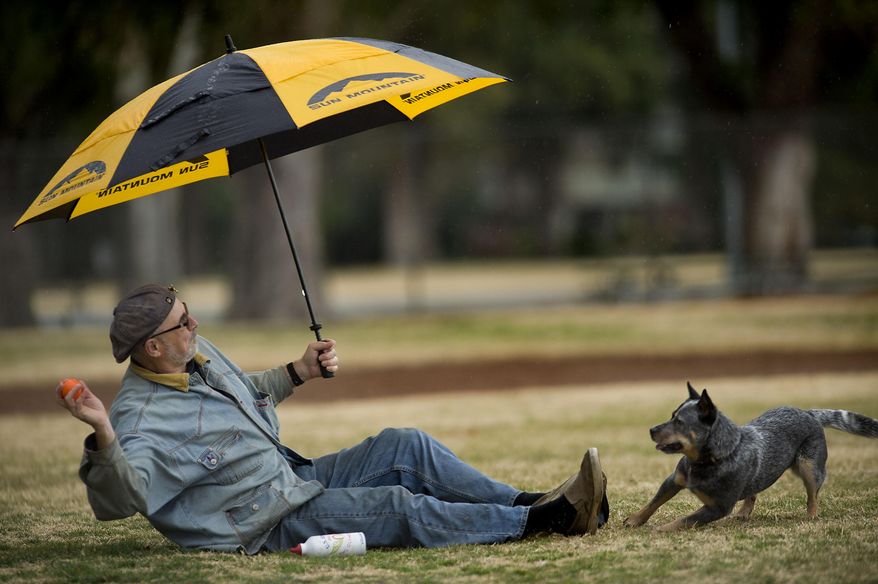 Bon Smith of Land Park area tosses a ball from under an umbrella for his dog 'Jesse' in William Land Park in Sacramento on Wednesday, Jan. 29, 2014. After a long dry season, rain finally fell in Sacramento. The National Oceanic and Atmospheric Administration's Web site is predicting a tenth of an inch of rain in San Francisco over the next two days and more than 2 inches in parts of Sacramento. (AP Photo/The Sacramento Bee, Randall Benton) MAGS OUT; LOCAL TV OUT (KCRA3, KXTV10, KOVR13, KUVS19, KMAZ31, KTXL40); MANDATORY CREDIT