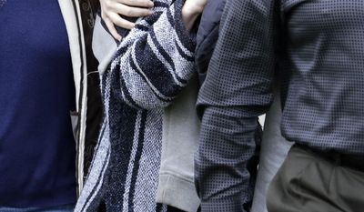 ADDS STATEMENT FROM KNOX SPOKESMAN DAVID MARRIOTT-An unidentified woman, center, is hidden under a jacket while being escorted from the home of Amanda Knox's mother, Thursday, Jan. 30, 2014, in Seattle.  Knox’s family spokesman, David Marriott, said Thursday that Knox was at the house when an Italian court upholding her murder conviction was read Thursday, but said he didn’t know whether the person who emerged was Knox. On Friday, Marriott stated he had made inquiries and that the person under the jacket wasn’t Knox. (AP Photo)