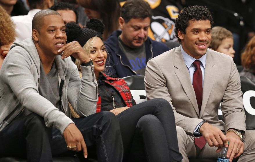 Rapper Jay Z, left, sits beside his wife Beyonce, and Seattle Seahawks quarterback Russell Wilson, right, as they watch the Brooklyn Nets NBA basketball game against the Philadelphia 76ers at the Barclays Center, Monday, Feb. 3, 2014 in New York. (AP Photo/Kathy Willens)