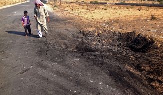 ** FILE ** In this Wednesday, Nov. 20, 2013, file photo, a man and child walk past a crater from a suicide car bomb attack on the road between the border town of Rafah and the coastal city of el-Arish, Egypt. (AP Photo/Ahmed Abu Deraa, File)