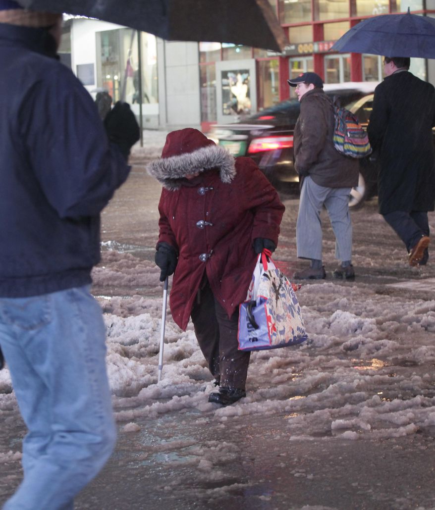A woman uses a cane to make her way through slush and puddles in New York's Times Square, Wednesday, Feb. 5, 2014. While New York City public schools remain open, there are transit delays in the area's subways, commuter rail lines and airports. (AP Photo/Mark Lennihan)