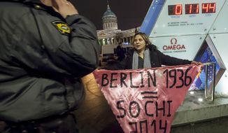 A gay rights activist holds a banner in front of a large clock showing the number of days left until the start of the Olympic games as a police officer approaches, left, in St. Petersburg, Russia, Wednesday, Feb. 5, 2014. Russian gay rights activists protested the upcoming Olympic Games in Sochi. Two activists unfurled banners reading “Berlin 1936 = Sochi 2014,” referring to the Olympic Games that were held in the capital of Nazi Germany. One-man pickets are legal in Russia and the two activists holding signs were spaced far enough apart that neither was arrested. (AP Photo/Elena Ignatyeva)