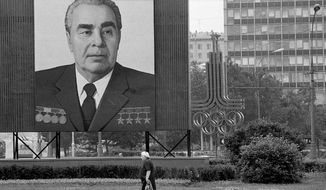 FILE - In this July 7, 1980 file photo, a woman walks past a huge portrait of Communist Party leader Leonid Brezhnev that dwarfs the symbol of the upcoming XXII Summer Olympics right behind, in Moscow. Brezhnev and his ruling Politburo wanted the games to legitimize the Soviet system, a military superpower and economic basket case. (AP Photo/File)