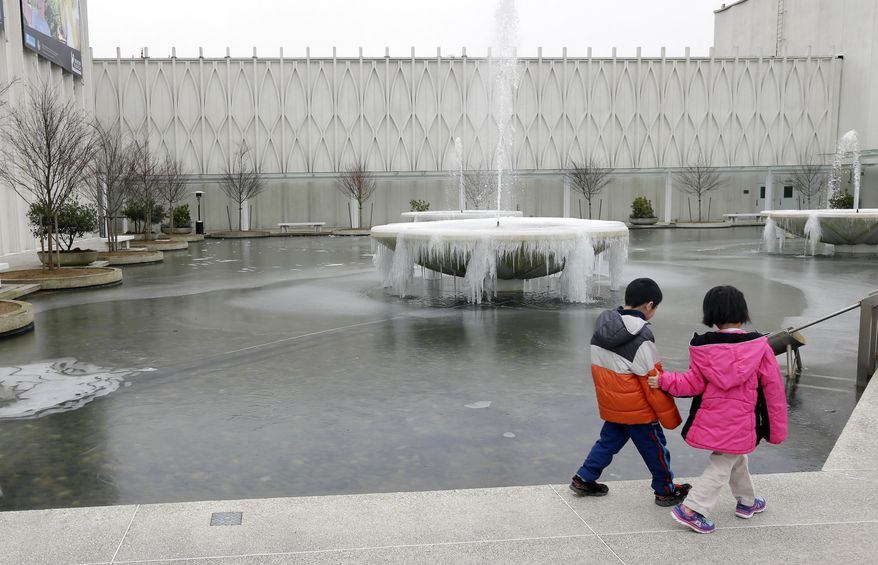 Two children on a school outing walk past a frozen fountain caked with ice at the Pacific Science Center in Seattle, Thursday, Feb. 6, 2014. Below-normal, frigid temperatures are forecast to continue into the weekend in Washington and then begin to moderate next week. (AP Photo/Ted S. Warren)