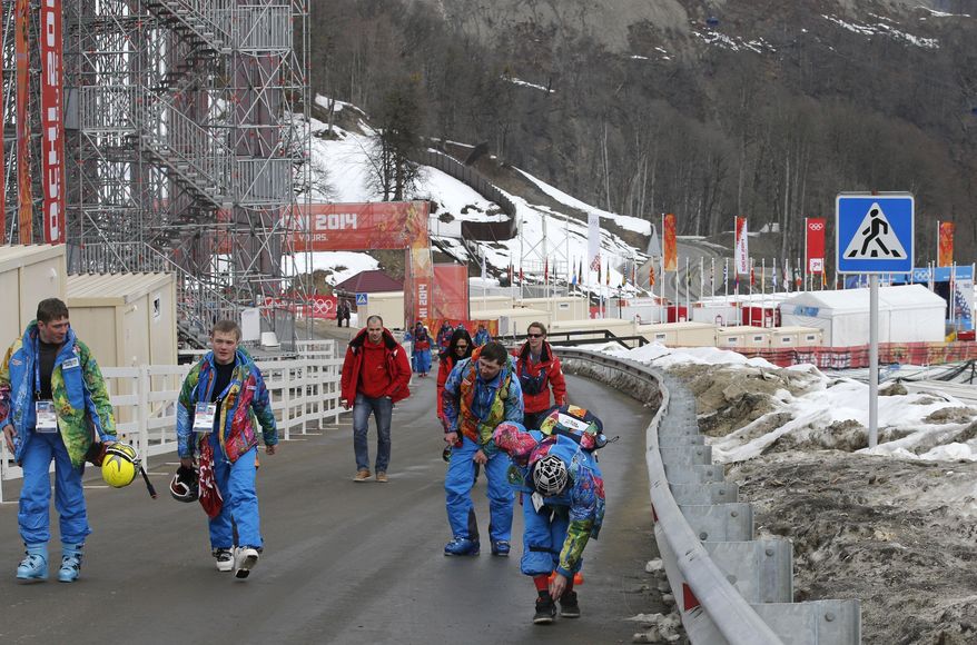 Course workers walk on the road behind the finish area of the alpine ski venue at the Sochi 2014 Winter Olympics, Tuesday, Feb. 11, 2014, in Krasnaya Polyana, Russia. Warm temperatures in the mountains was a factor in the cancellation of Women's downhill training on Tuesday. (AP Photo/Christophe Ena)