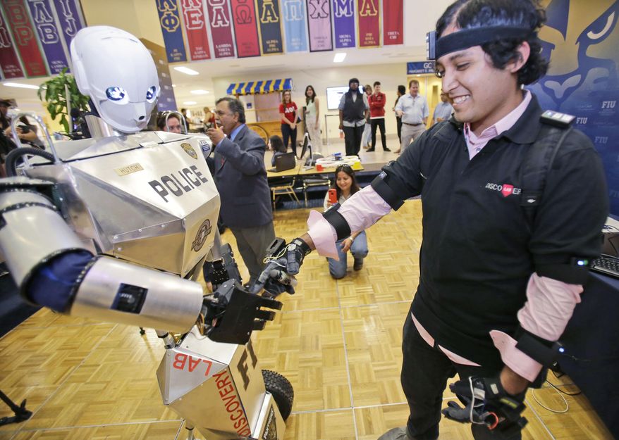 Student Irvin Cardenas, right, 22, shakes hands with a TeleBot, which combines telepresence and robotics, as he controls its movements with sensors placed around his body, during a demonstration at Florida International University, Wednesday, Feb. 12, 2014 in Miami. A group of students at FIU's Discovery Lab is testing their version of a RoboCop that will allow disabled police and military personnel to serve as patrol officers. The robot imitates all of the movements of the demonstrator, the student in this case, police or military officers in the future, who is wearing about 30 sensors on their shoulders, elbows, head and fingers. A joystick moves the robot forward, back and in circles. (AP Photo/Wilfredo Lee)