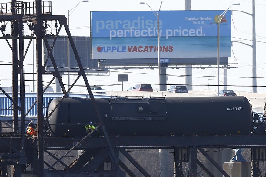 FILE - In this Jan. 24, 2014, file photo, cars pass railroad crews working on one of six tank cars carrying oil from North Dakota that derailed near the heart of Philadelphia on a bridge above the Schuylkill River. Although no oil was spilled, the accident rattled nerves. Industry experts say trains carrying crude and other flammables are likely to continue rolling through major cities despite pressure to steer the potentially-explosive shipments around population centers. (AP Photo/Matt Rourke, File)
