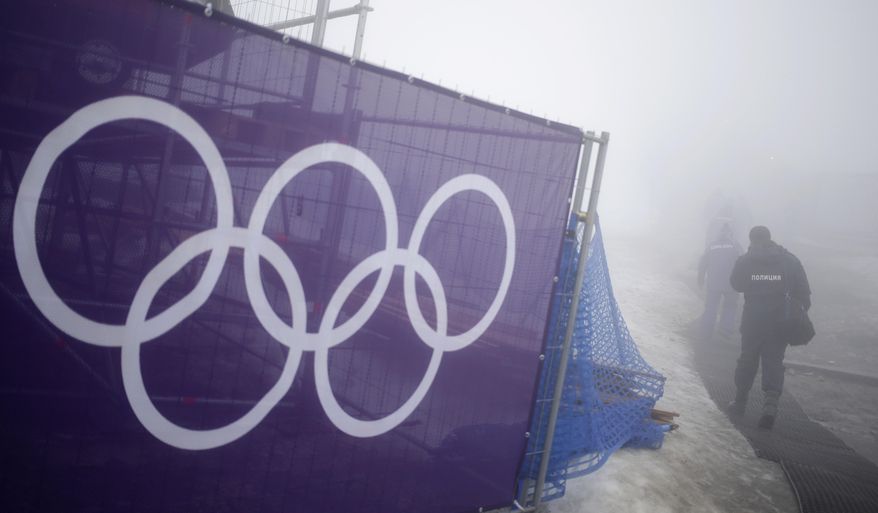 Security guards walk past the Olympic rings prior to a men's snowboard cross competition at the Rosa Khutor Extreme Park, at the 2014 Winter Olympics, Monday, Feb. 17, 2014, in Krasnaya Polyana, Russia. (AP Photo/Andy Wong)