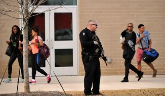 Students leave campus behind an armed police officer after a youth with two pistols was apprehended near the front of Chamblee Charter High School, according to authorities, on Tuesday, Feb. 18, 2014, in Chamblee, Ga., a suburb northeast of Atlanta. Chamblee City Manager Marc Johnson said a 16-year-old boy that had been suspended from the school was arrested without incident and police found a stash of additional weapons in the nearby woods, allegedly from a burglary earlier in the day. (AP Photo/David Tulis)