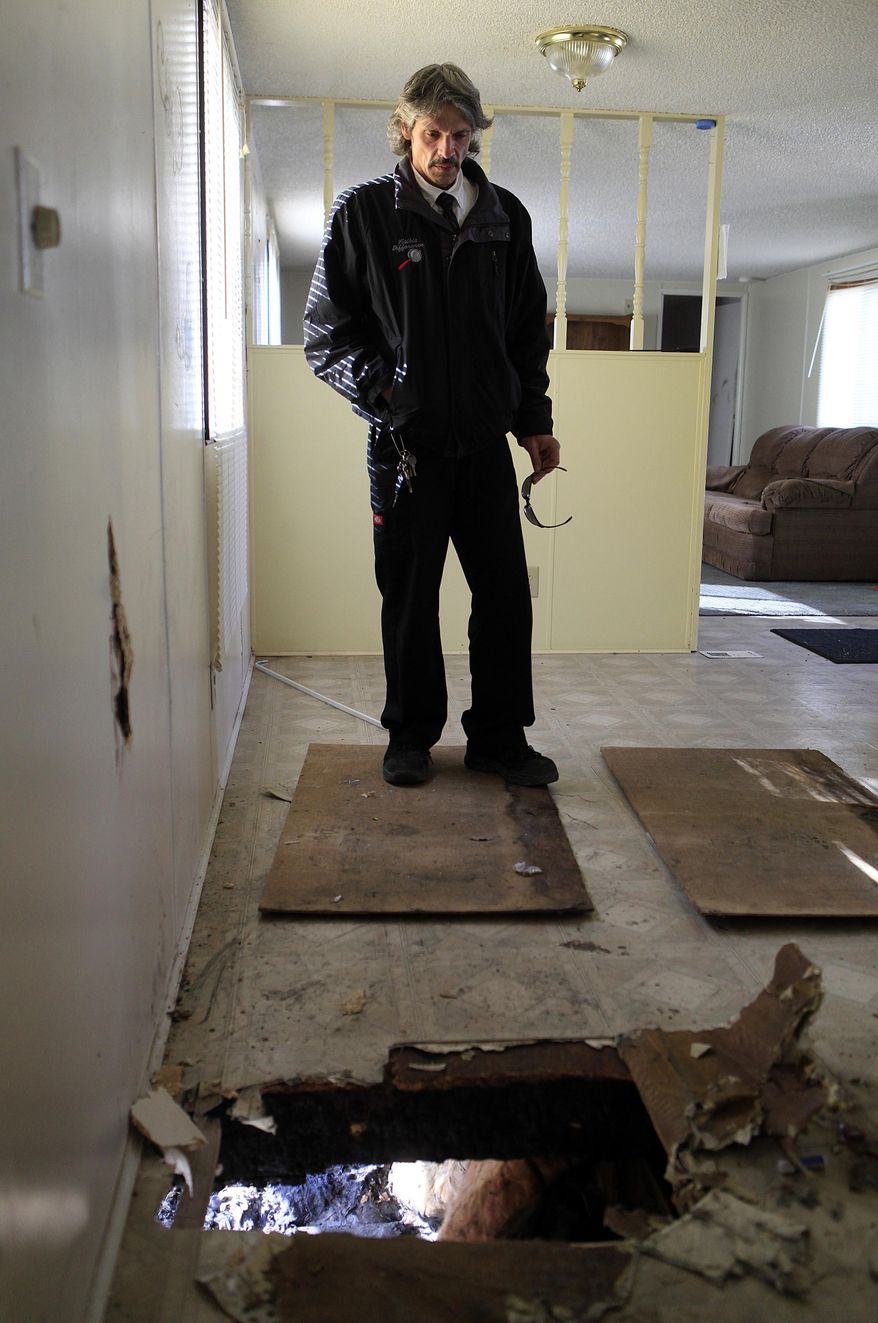 Dave Tolley looks at a hole in his kitchen caused by a fire that started below his trailer home at Wheel Estates on Feb. 18, 2014 in Rapid City, S.D. Tolley believes lingering sewer and water issues caused the home to settle and may have contributed to the fire. (AP Photo/Raid City Journal, Chris Huber)