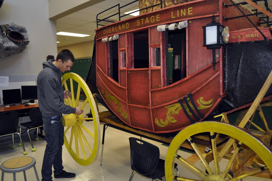 In this Feb. 4, 2014 photo, Powell High School art student Austin Ouellette places a wheel on a replica of the Concord stagecoach created by art students, in Powell, Wyo. Once finished, the stagecoach will be on display in the Powell High School library. (AP Photo/The Powell Tribune, Tessa Schweigert)